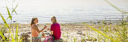 Zwei Frauen picknicken gemeinsam am Ostseestrand.  - zum Artikel 'Tourismus in Schleswig-Holstein erholt sich weiter'