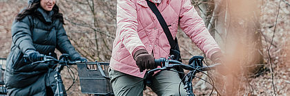 Zwei Frauen fahren Rad auf einem Radweg im Naturpark Lauenburgische Seen. Sie lächeln und betrachten die Umgebung. Im Hintergrund liegt der karge Wald. Die Frauen tragen warme Kleidung.  - zum Artikel 'Zur Buchungslage 2021 in Schleswig-Holstein'
