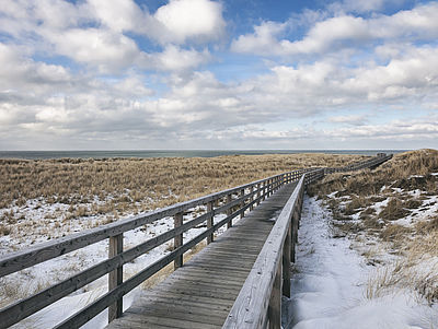 Holzsteg zwischen verschneiten Dünen