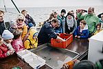 Eine Gruppe von Kindern und Erwachsenen steht dicht gedrängt auf einem Forschungsschiff an Deck. Sie beobachten aufmerksam einen Mann in dunkelblauer Kleidung, der aus einer roten Kiste Meereslebewesen entnimmt und zeigt.