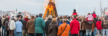 Menschen stehen um ein Osterfeuer an der Flensburger Förde.  - zum Artikel 'Ostern wird bunt in Schleswig-Holstein!'