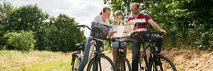 Ein Mann, eine Frau und ein Junge stehen mit ihren Fahrrädern auf einem Weg und schauen in eine Radkarte.  - zum Artikel 'Auf zwei Rädern durchs Land'