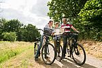Ein Mann, eine Frau und ein Junge stehen mit ihren Fahrrädern auf einem Weg und schauen in eine Radkarte. 