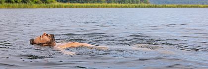 Ein Mann liegt in Badehose in einem See und lässt sich treiben. Sein Gesicht ist dem Himmel zugewandt und die Augen sind geschlossen. - zum Artikel 'Pack‘ die Badehose ein: Ab zum See in Schleswig-Holstein'