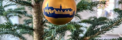 Eine goldene matte Weihnachtskugel hängt in einem Weihnachtsbaum. Die Weihnachtskugel ziert das Motiv des Plöner Schlosses in dunkler Silhouette. .  - zum Artikel 'Schöne Bescherung mit regionalen Produkten aus Schleswig-Holstein'