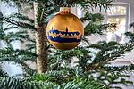 Eine goldene matte Weihnachtskugel hängt in einem Weihnachtsbaum. Die Weihnachtskugel ziert das Motiv des Plöner Schlosses in dunkler Silhouette. . 