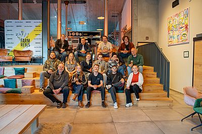 Gruppenfoto von etwa 20 Personen auf Holzstufen in Brauerei-Atmosphäre mit „Farm Rebels“-Banner im Hintergrund.