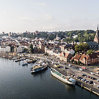 Luftaufnahme von Urlaubsort Flensburg in Schleswig-Holstein mit Blick auf den Hafen, Schiffe am Kai, die Altstadt mit roten Ziegeldächern und Kirchtürmen.