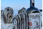 Eine Flasche des Gins "Kel 1872" steht angelehnt an Treibholz am Strand von Kellenhusen. 