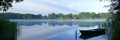 Ein kleines Boot liegt auf einem stillen See, in dem sich die umliegende Natur und der Himmel spiegeln.  - zum Artikel 'Unbekannte Ostsee'