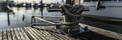 Ein Steg an der Kiellinie und im Hintergrund liegen Segelschiffe auf dem Wasser. - zum Artikel 'Meeting- & EventBarometer 2023/2024 sieht Schleswig-Holsteins Tagungssegment auf positivem Kurs'