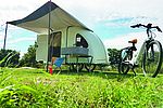 Ein kleiner Campingwagen mit Vorzelt steht auf einer Wiese. Davor gespannt ist ein Fahrrad. 