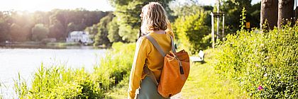 Eine Frau steht mit einem Rucksack auf einem Weg und schaut auf einen See. - zum Artikel 'Schätze suchen in Schleswig-Holstein – Auf Geocaching-Abenteuer '