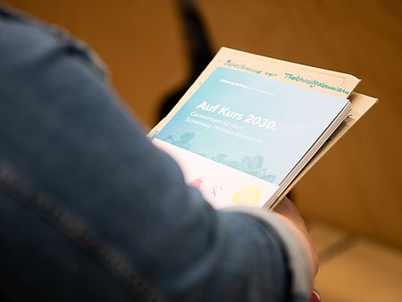 Eine Person hält eine Broschüre mit dem Titel „Auf Kurs 2030. Gemeinsam für den Schleswig-Holstein-Tourismus“ in der Hand.