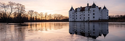 Das historische Wasserschloss in Glücksburg im Licht der untergehenden Wintersonne. Auf dem Schlossteich bildet sich eine Eisfläche. - zum Artikel 'Traumhafte Einblicke in das Leben des Adels an Nord- und Ostsee'
