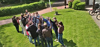 Gruppe von Menschen hält gemeinsam eine lange Stange bei einer Teambuilding-Übung im Freien.