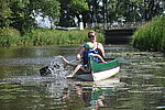 Eine Frau in einem grünen Kanu paddelt durch die Wilsterau im Holsteiner Auenland in der Nähe von Itzehoe. Vorn im Kanu sitzt ein Kind und planscht mit den Füßen im Wasser. 