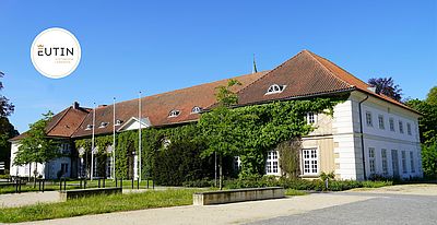 Historisches Gebäude in Eutin mit rotem Dach, weißer Fassade und Efeubewuchs bei blauem Himmel.