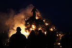 Ein großes Biikefeuer brennt. Im Vordergrund des Feuers befinden sich die Silhouetten von Menschen. 