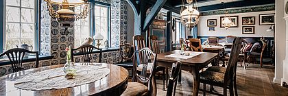 Auf dem Bild sind historische dunkle Esszimmermöbel in einem Raum abgebildet. Tische, Stühle und Leuchter, auf den Tischen liegen gehäkelte Tischdecken. In den Räumlichkeiten des Hans-Momsen-Hauses kann heute Kaffee getrunken werden. Außerdem können Gäste an einer Führung teilnehmen.  - zum Artikel 'Cafés mit Torte und Historie in Schleswig-Holstein'