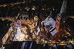 Luftaufnahme vom Maritimen Weihnachtsmarkt auf dem Koberg in Lübeck. Der Weihnachtsmarkt ist hell erleuchtet bei dunklem Himmel. Neben einem Riesenrad ist links die Jakobikirche zu sehen. Es liegt wenig Schnee auf den Dächern.