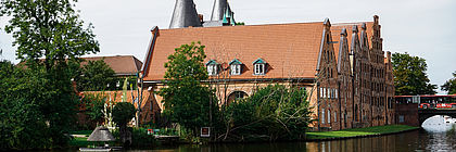 Die Salzspeicher in Lübeck an der Trave. Im Hintergrund ist das Holstentor erkennbar. Auf der Trave fährt ein Kajak. - zum Artikel 'Summer in the City'