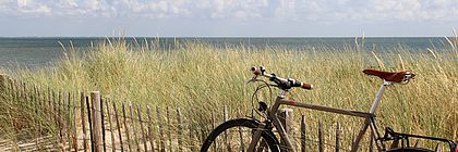 Ein Fahrrad lehnt an einem Zaun am Strand. - zum Artikel 'Radfahren in Schleswig-Holstein – neue Online-Kampagne wirbt für das Trendthema im echten Norden'