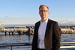 Ein nMann in Businesskleidung steht an der Kieler Förde und schaut in die Kamera.
