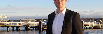 Ein nMann in Businesskleidung steht an der Kieler Förde und schaut in die Kamera. - zum Artikel 'Patrick Marks neuer Leiter Digitales Management der Tourismus-Agentur Schleswig-Holstein in Kiel'