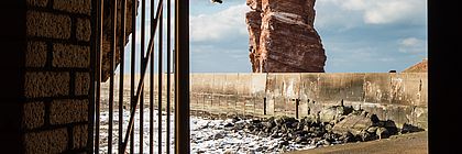 Der Blick führt durch ein geöffnetes Tor direkt auf einen hohen Felsen aus rotem Sandstein.  - zum Artikel 'Von Legenden umrankt: Sagenumwobene Orte im echten Norden'