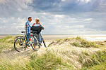 Zwei Personen stehen mit ihren Fahrrädern auf einer Düne am Strand von Föhr. Die Nordsee ist im Hintergrund zu sehen. 
