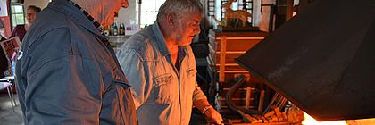 Zwei Männer stehen in der Schmiede vor offenem Feuer. - zum Artikel 'Altes Handwerk in Schleswig-Holstein'