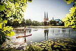 Eine Person fährt auf einem SUP auf dem Mühlenteich. Im Hintergrund ist der Dom zu Lübeck zu sehen. 