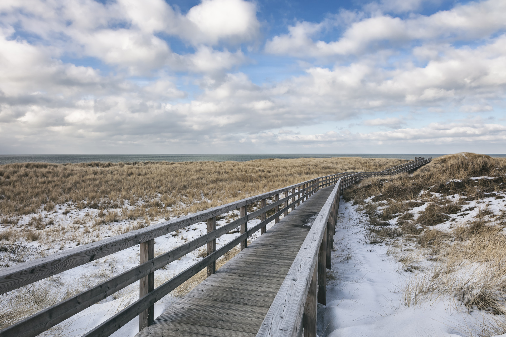 Holzsteg zwischen verschneiten Dünen
